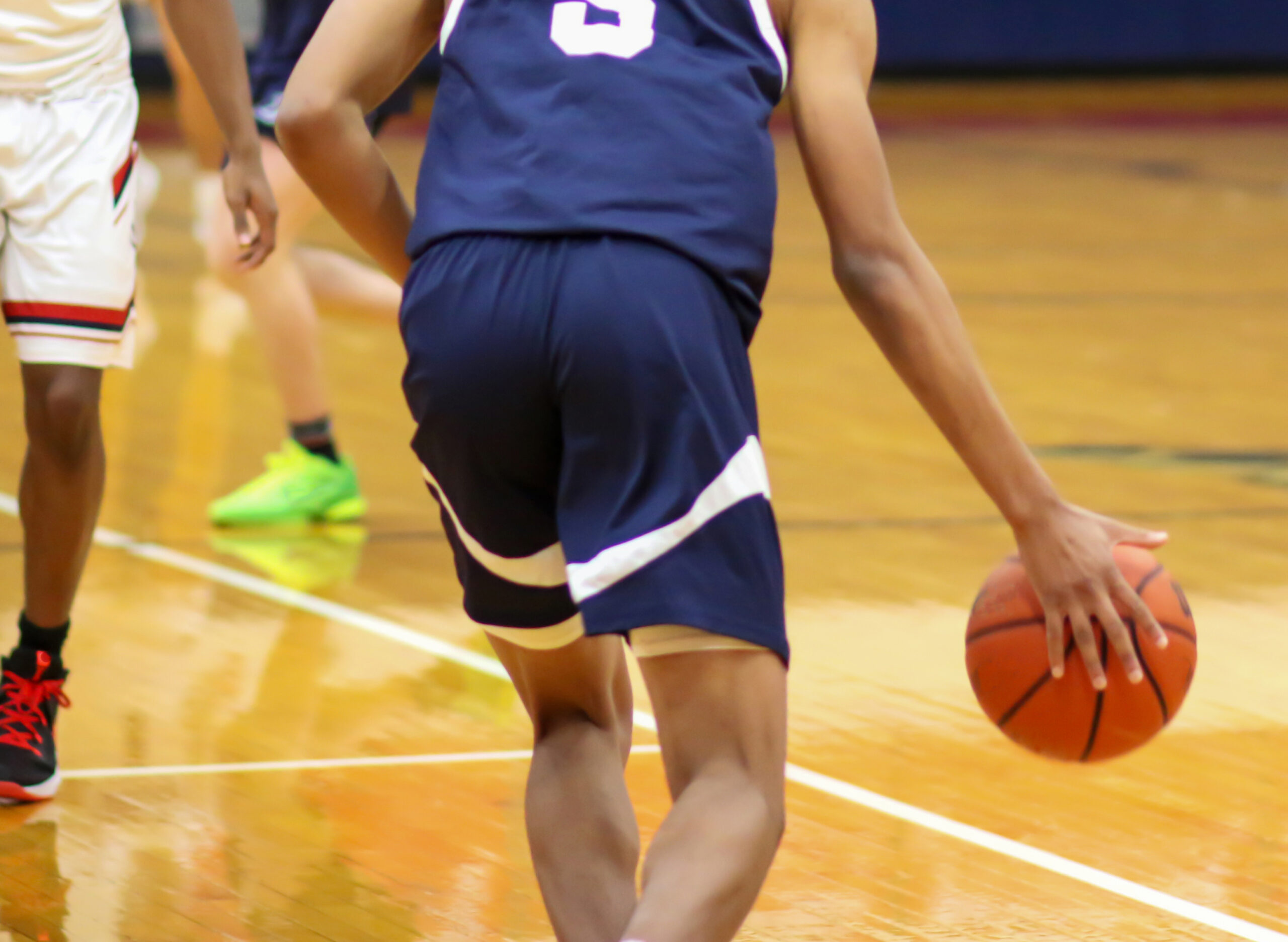 Rear view of a high school basketball player dribbling the ball up court during a varsity game close up.