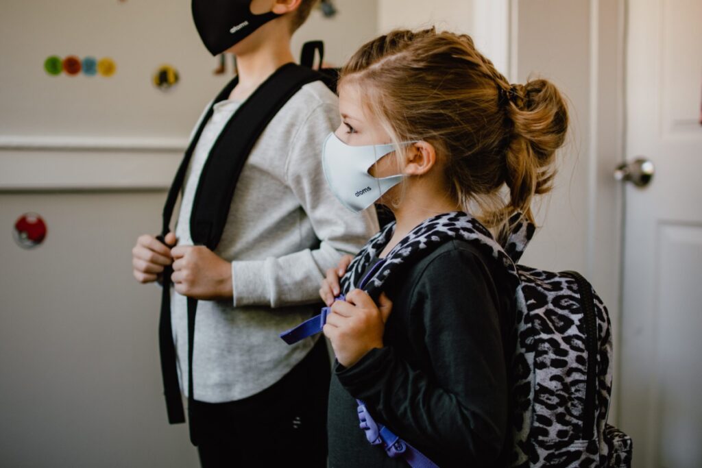 two children in a home with backpacks and masks preparing for to leave for school