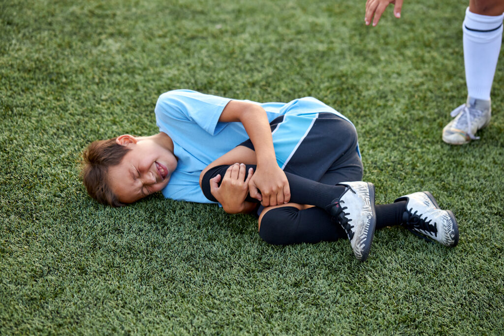 Little boy holding his knee on the ground during sport competition