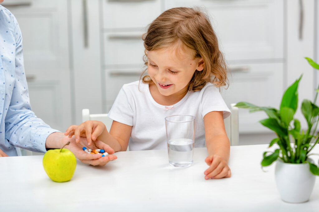 A small smiling child with pills taking medications or vitamin food supplements.
