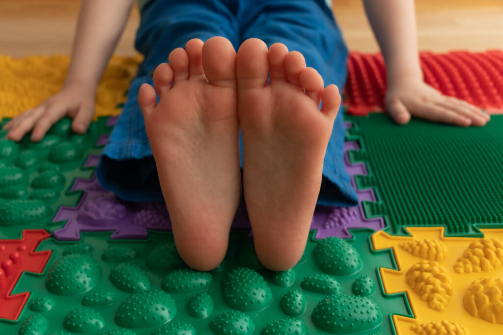 Baby sitting on massage mats, feet closeup. Healthy childhood.
