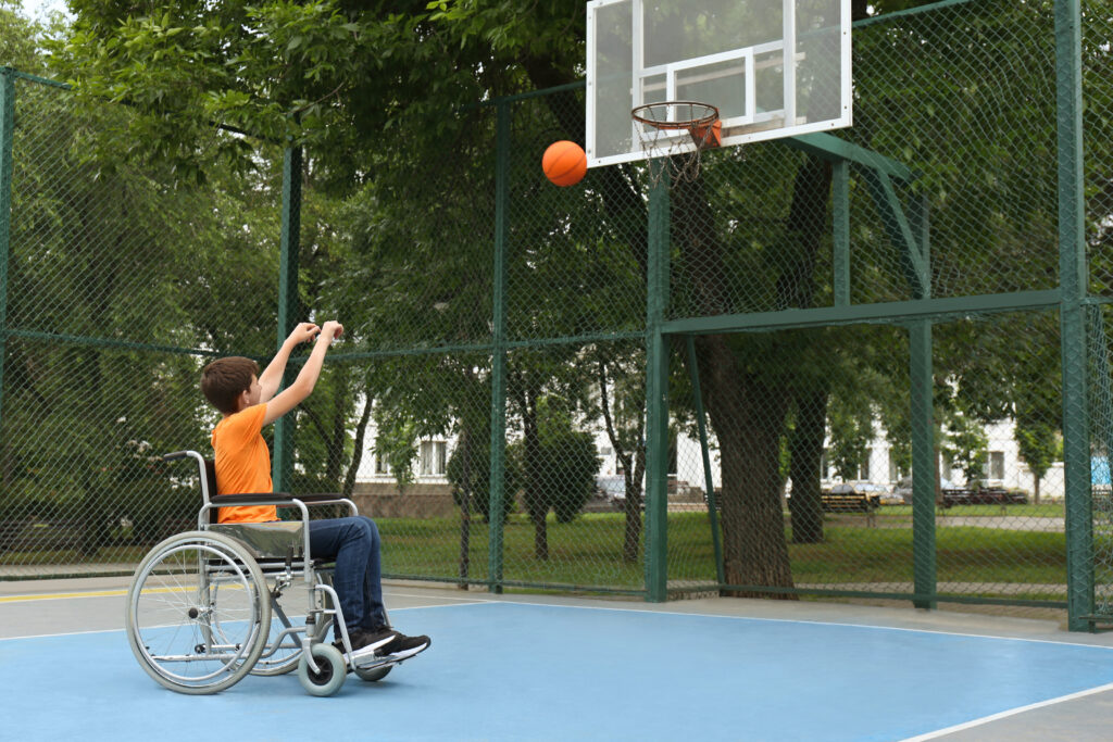 Disabled teenage boy in wheelchair playing basketball on outdoor court