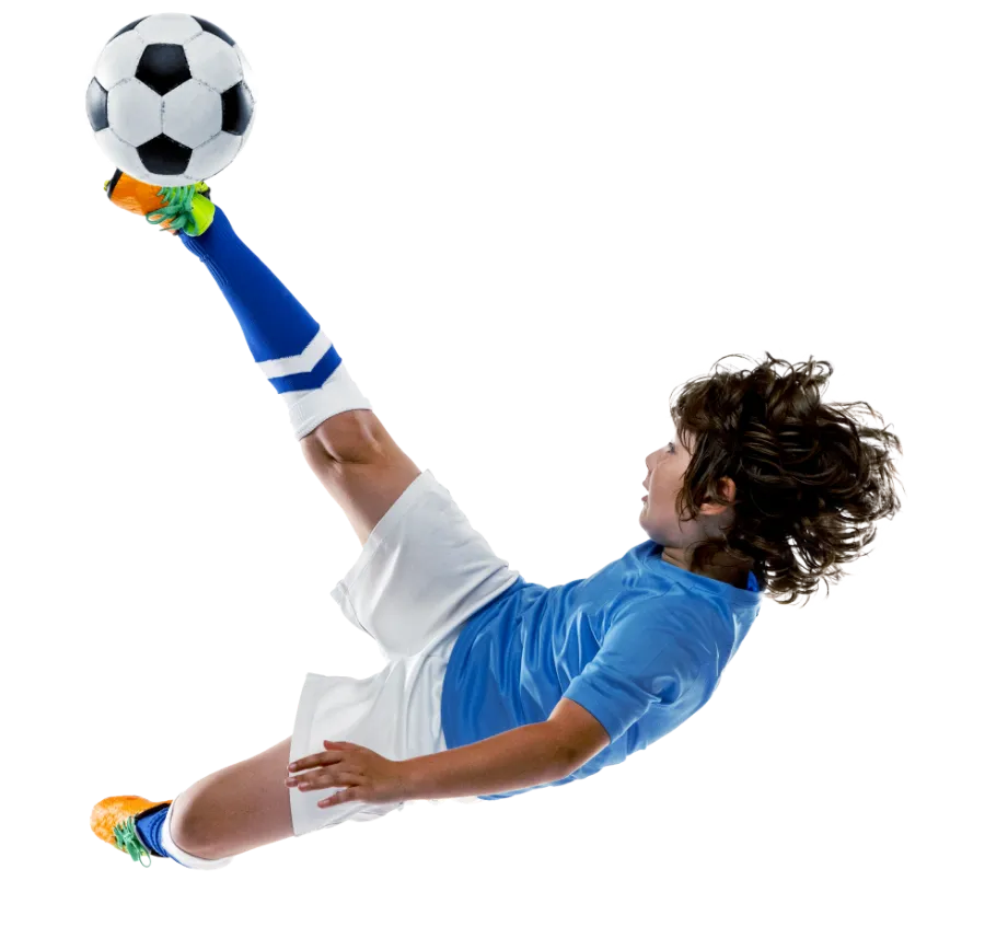 boy in soccer uniform jumping and kicking a ball in the air