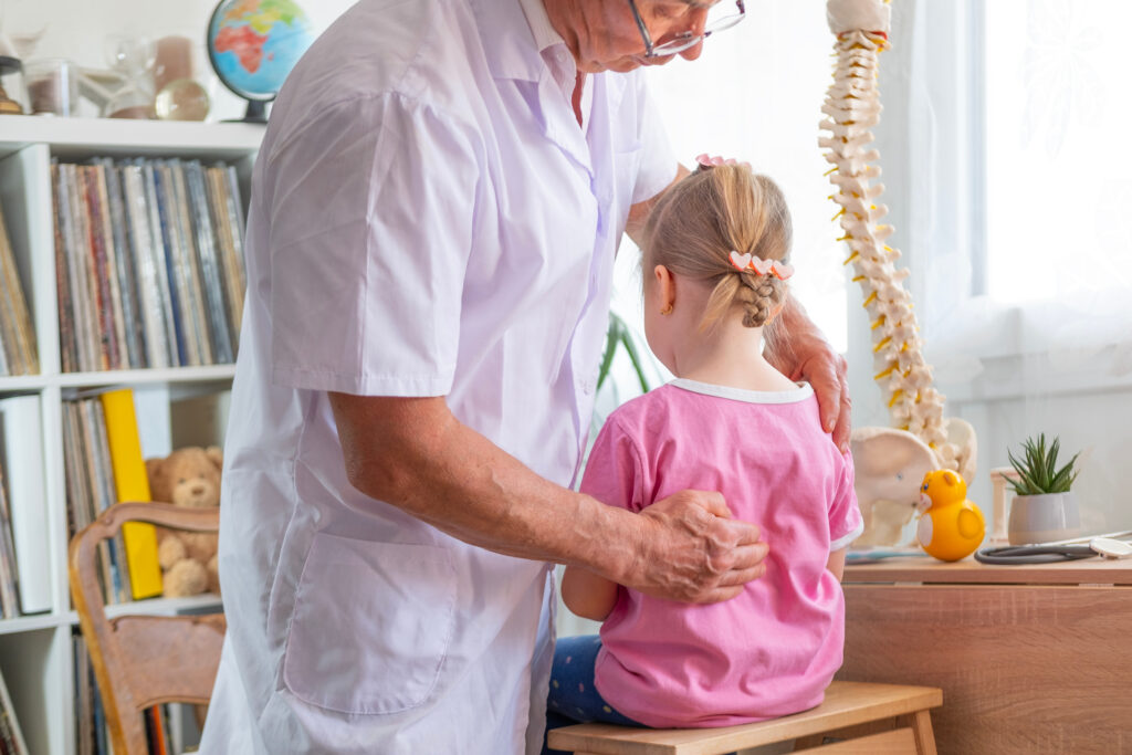 male Orthopedist doctor examining child's back in clinic, physician checks girl's spinal alignment, doctor conducting diagnostics and treatment scoliosis in children, health insurance